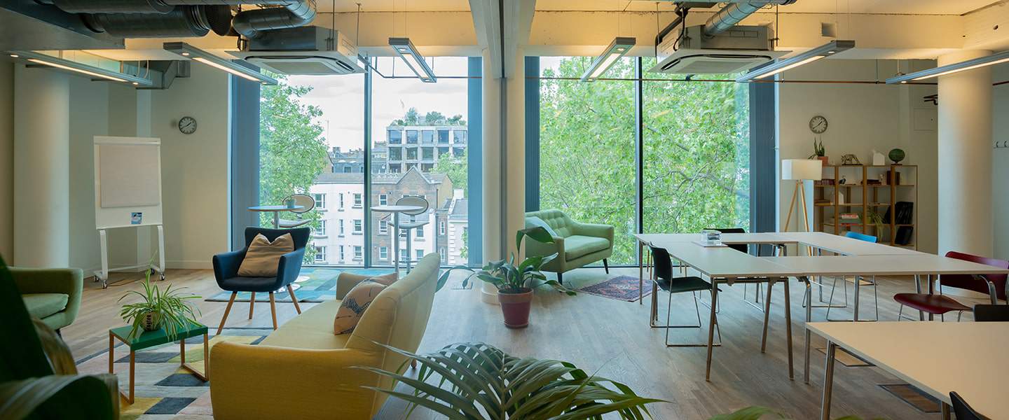 Tables and soft seating beside tall windows and exposed brickwork.